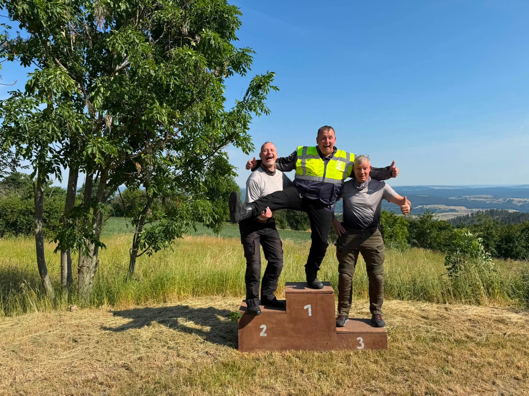 Drei Teilnehmer der Motorradtour scherzen gemeinsam auf einem Siegerpodest